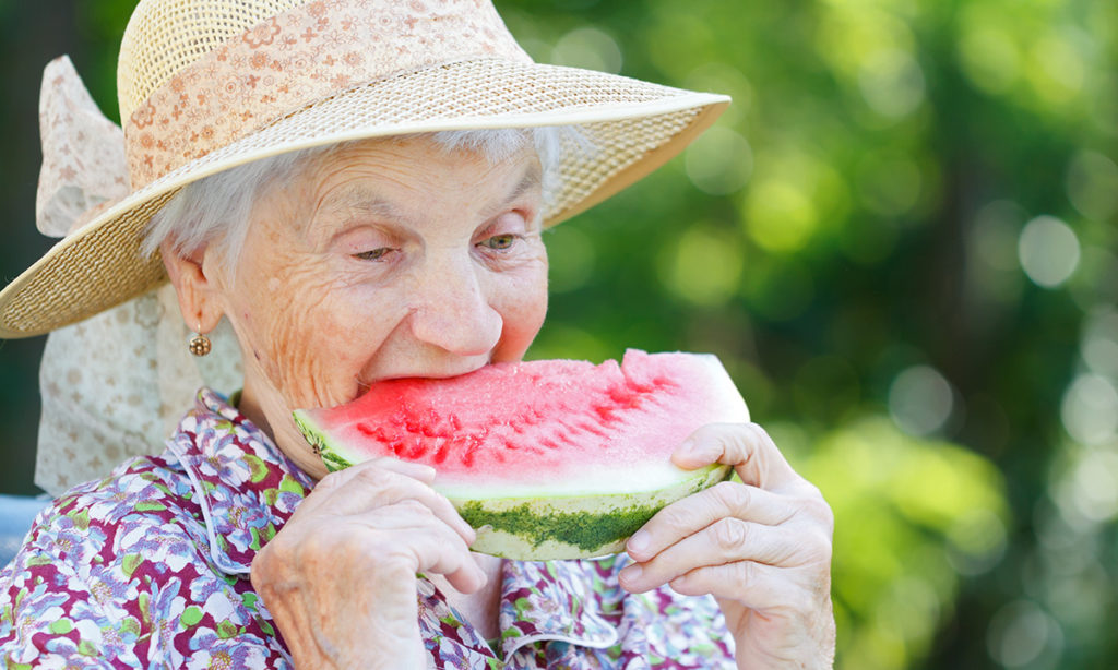Elderly woman eating watermellon.